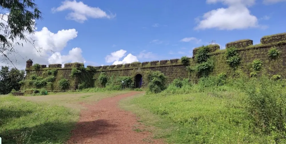 The laterite walls of Corjuem Fort with a dirt path through green grass