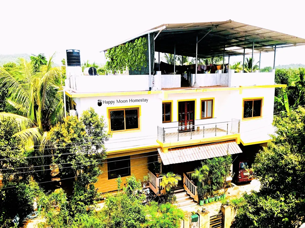 Happy Moon Homestay, a three-storey white and yellow house surrounded by palms